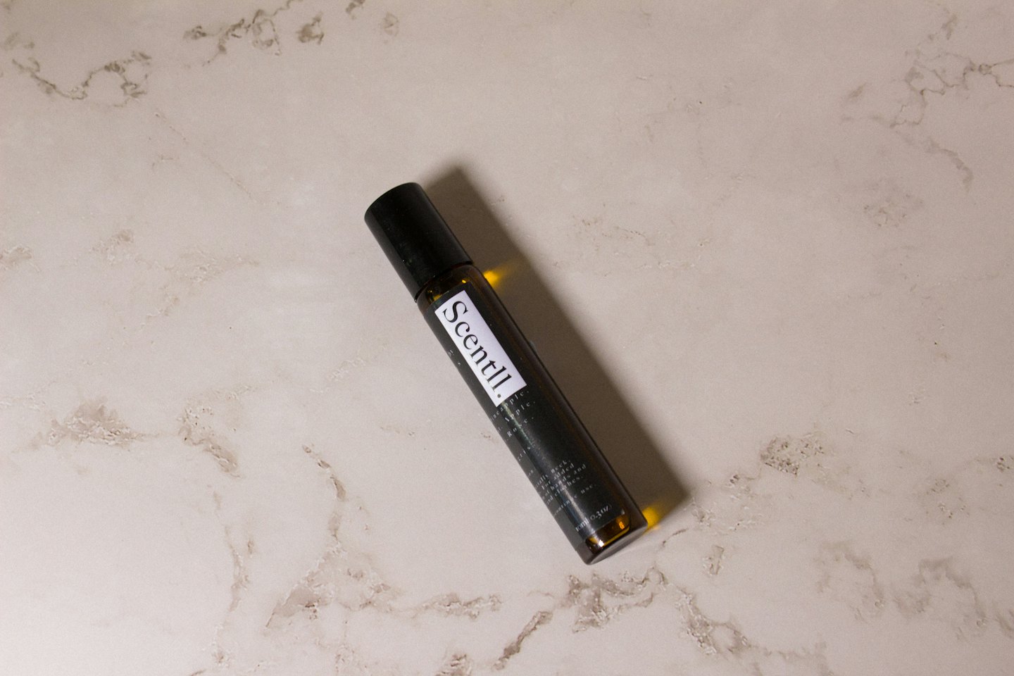 Amber glass roll-on bottle on veined marble surface.