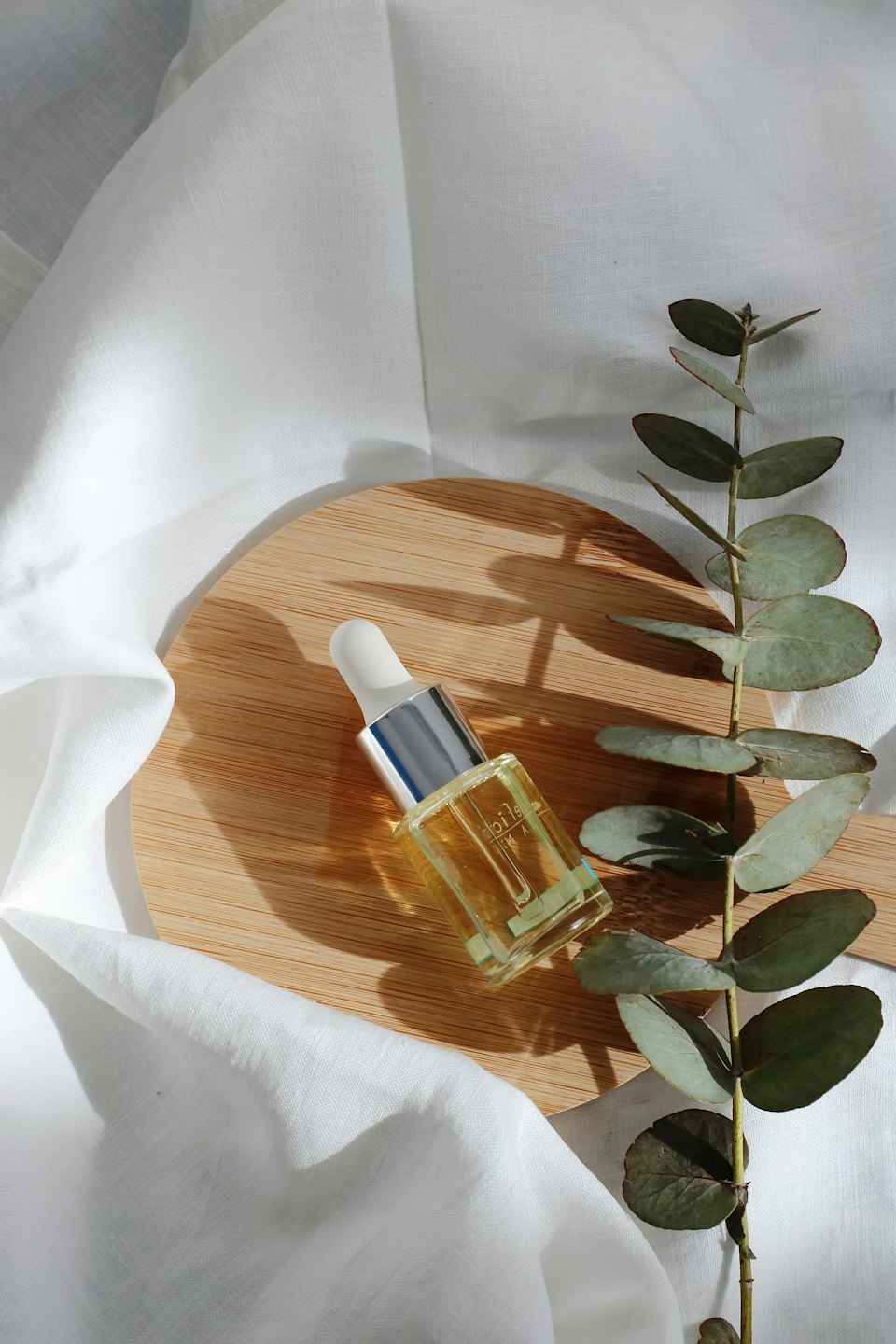 Glass dropper bottle with golden oil on wood and linen with eucalyptus.
