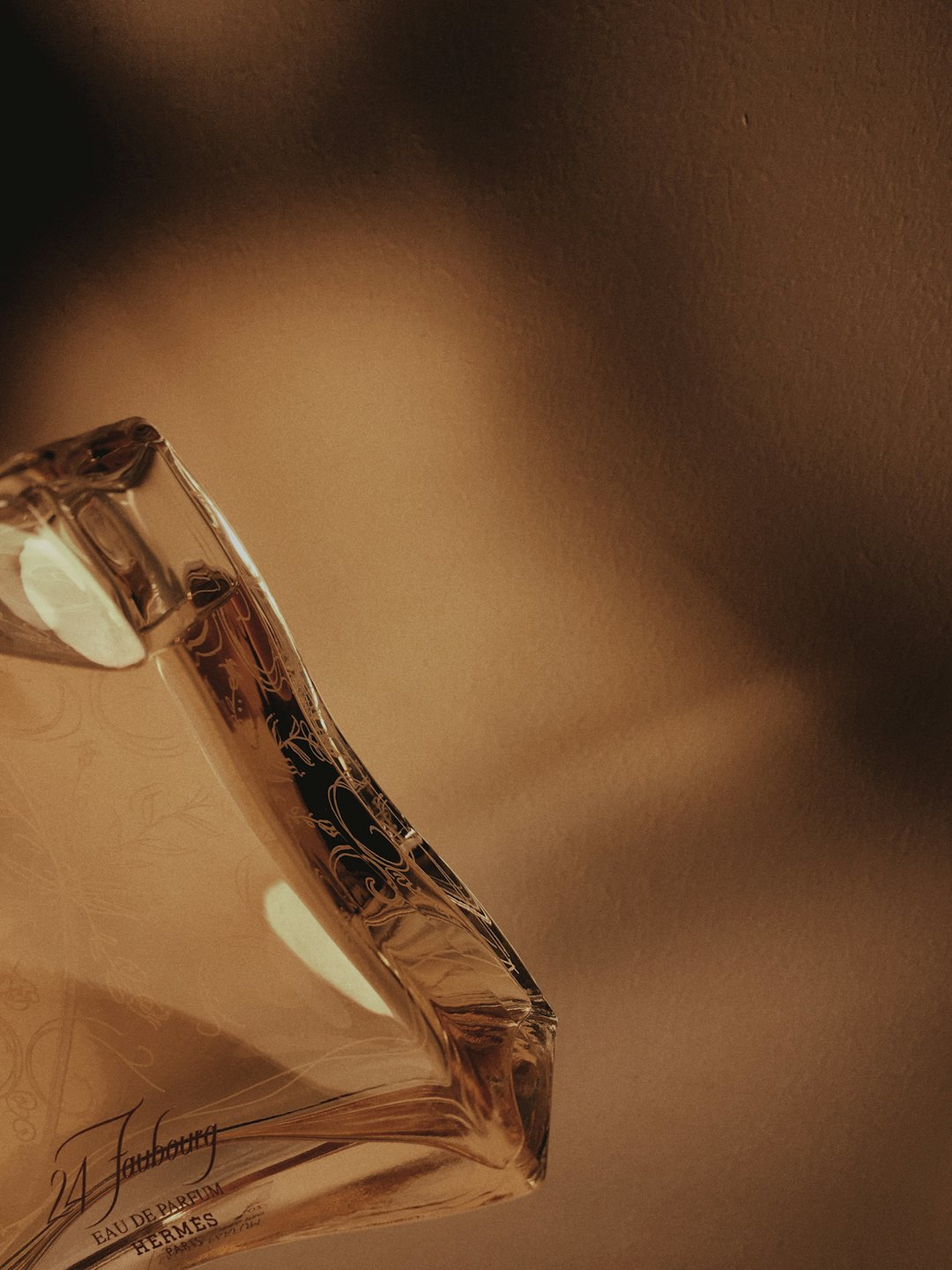 Clear glass perfume bottle with engraved details on a beige surface.