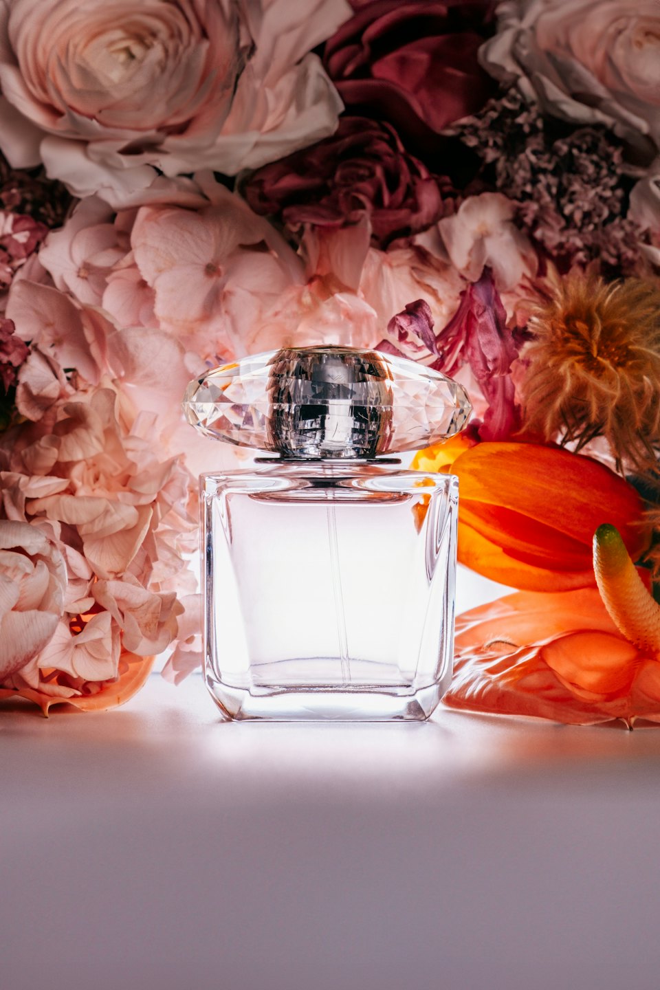 Glass perfume bottle with diamond cap sitting before floral bouquet.